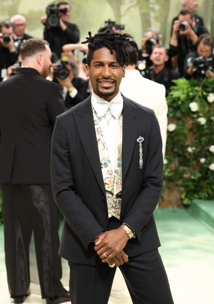 Jon Batiste in a suit with a floral shirt posing for photographers at an event