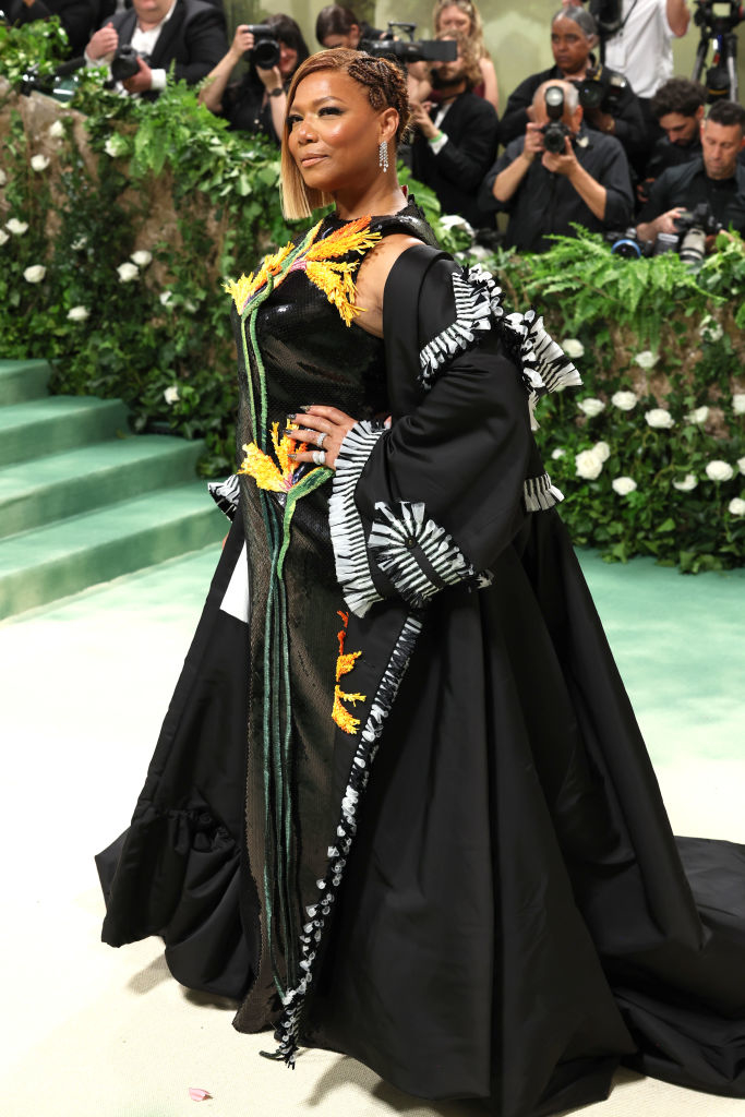 Queen Latifah in a black gown with embroidered details at an event with photographers in the background