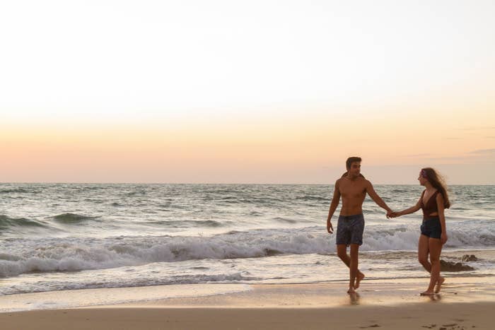 Two people holding hands and walking on a beach with waves in the background