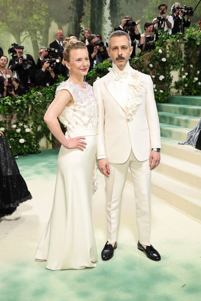 Emma in an embellished gown, Jeremy in suit with ruffled detail. Photographers in background