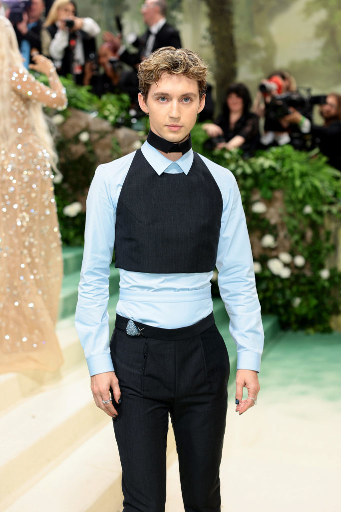 Troye Sivan in unique black and blue layered outfit on event carpet; photographers in background