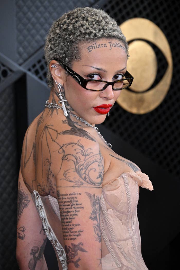 Woman with short hair and tattoos posing in sheer dress with visible undergarments