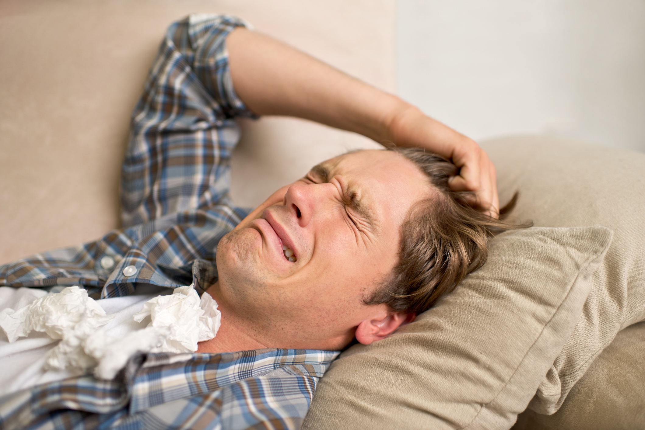 Person lying on a couch appearing to be ill with tissues nearby