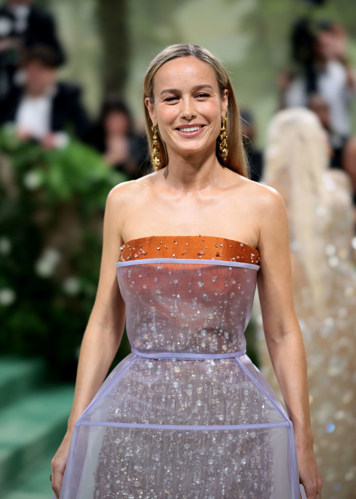 Brie Larson in a strapless, transparent gown with sparkling details, smiling on the red carpet