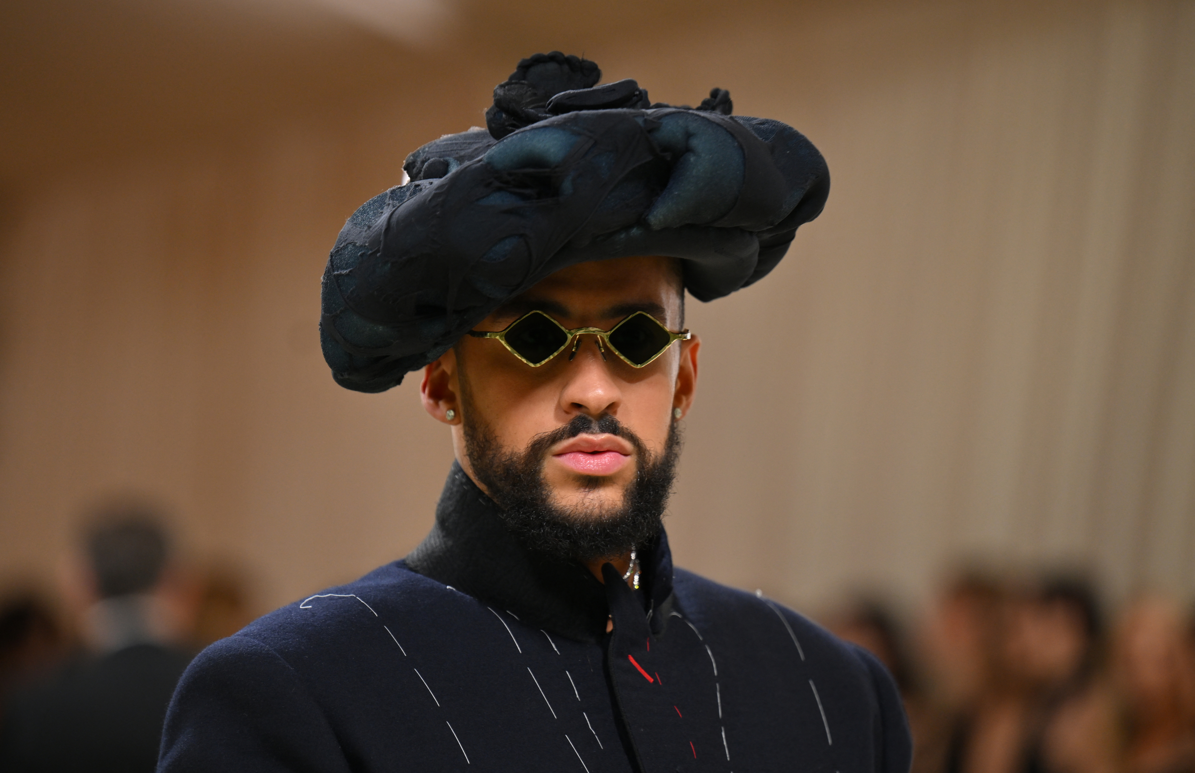 Bad Bunny in avant-garde hat and sunglasses with a structured jacket