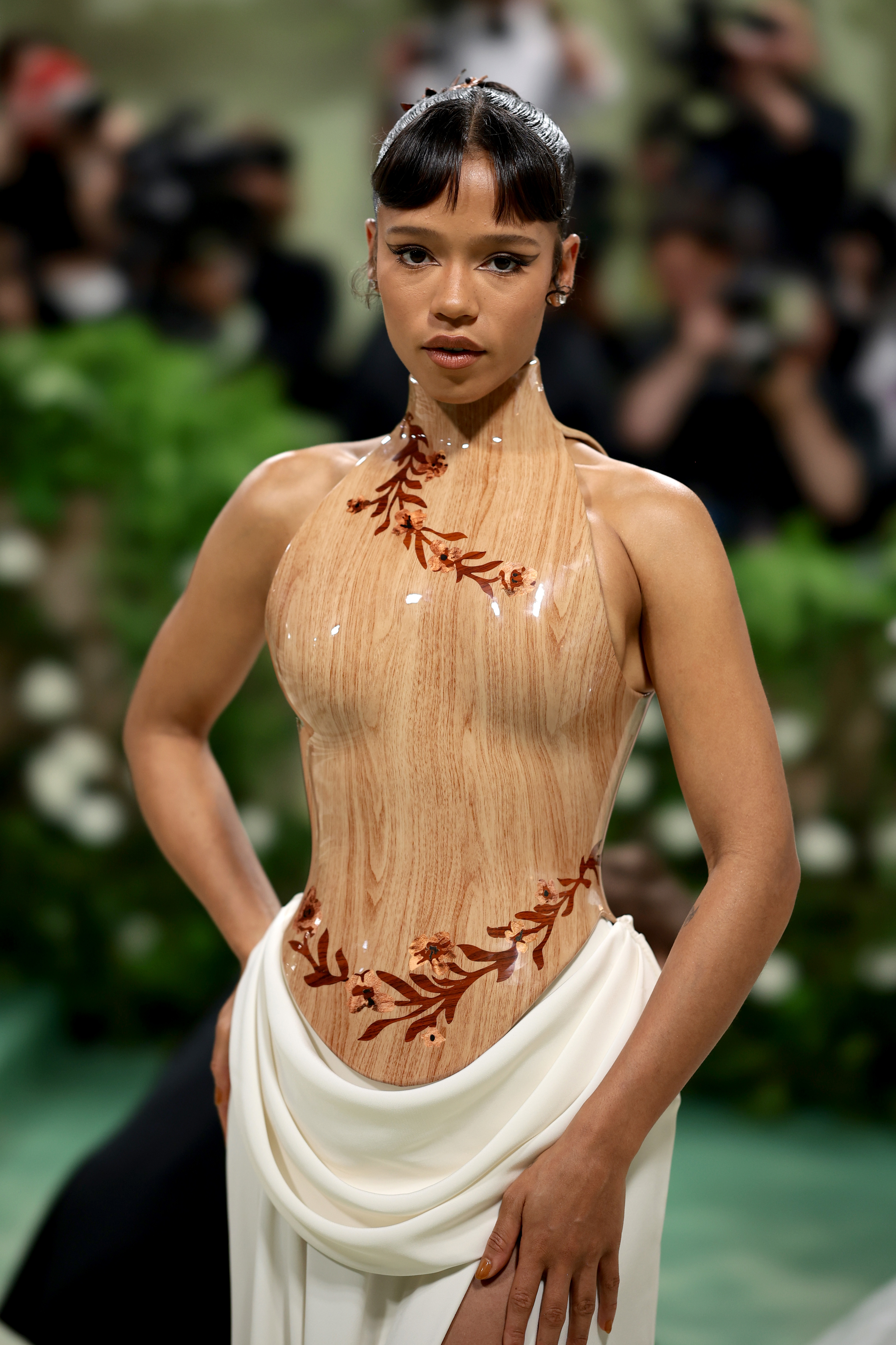 Taylor Russell in elegant dress with unique sheer top and solid bottom, posing on a carpeted area with cameras in the background