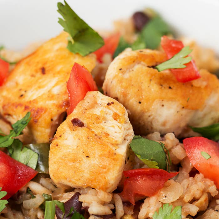 Grilled chicken pieces on rice with fresh herbs and chopped tomatoes