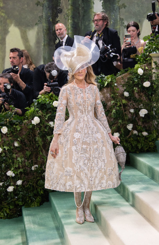 Sarah in elegant lace dress and large hat posing on steps at event, photographers in background