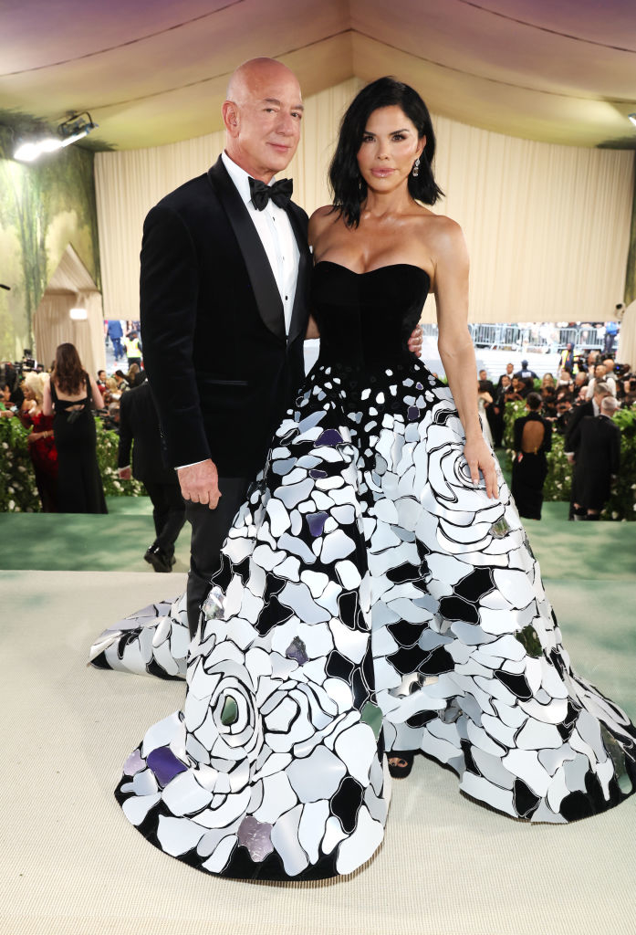 Jeff Bezos and Lauren Sanchez at an event. Sanchez wears a gown with floral design; Bezos in a classic tuxedo