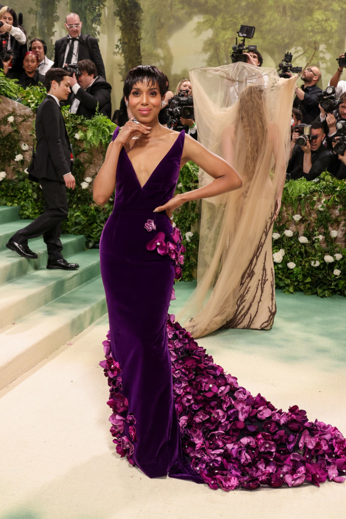 Kerry Washington poses in a purple gown with floral detail at an event, photographers in background