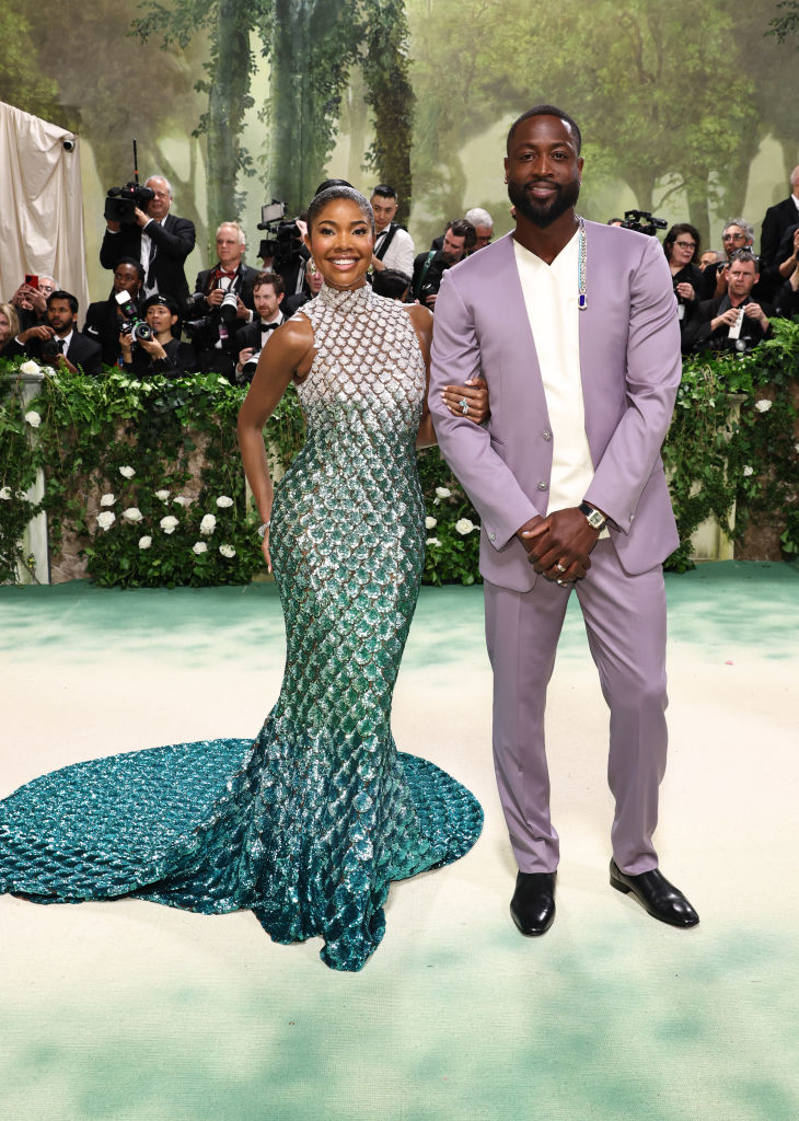Gabrielle Union in a scale-patterned gown with a train and Dwyane Wade in a pastel suit on a themed event backdrop