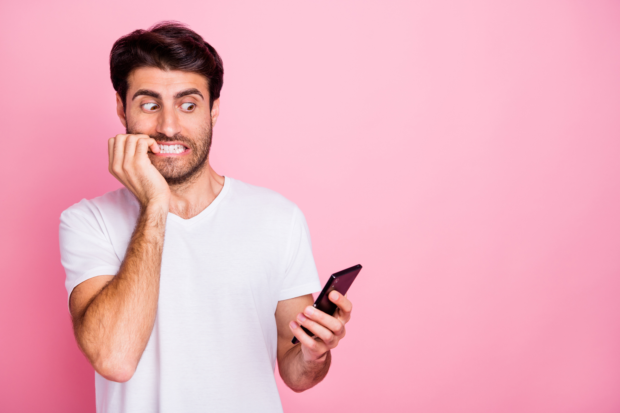 Man looking at smartphone with anxious expression, biting fingernails