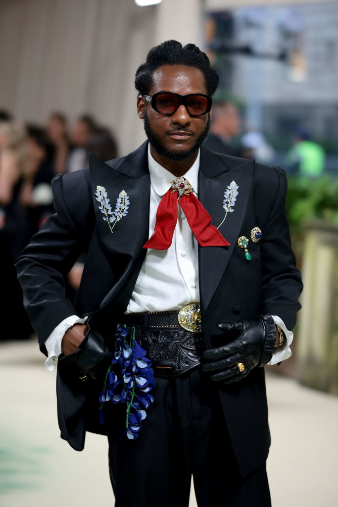 Leon Bridges in a black suit with ornate brooches and a belt; poses with confidence