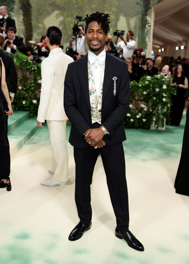 Jon Batiste in a black suit with a floral vest at a gala event