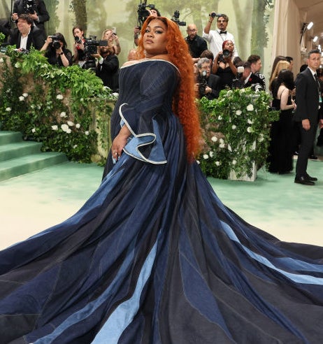 Da'Vine Joy Randolph in a flowing dark dress with a long train posing on stairs at an event