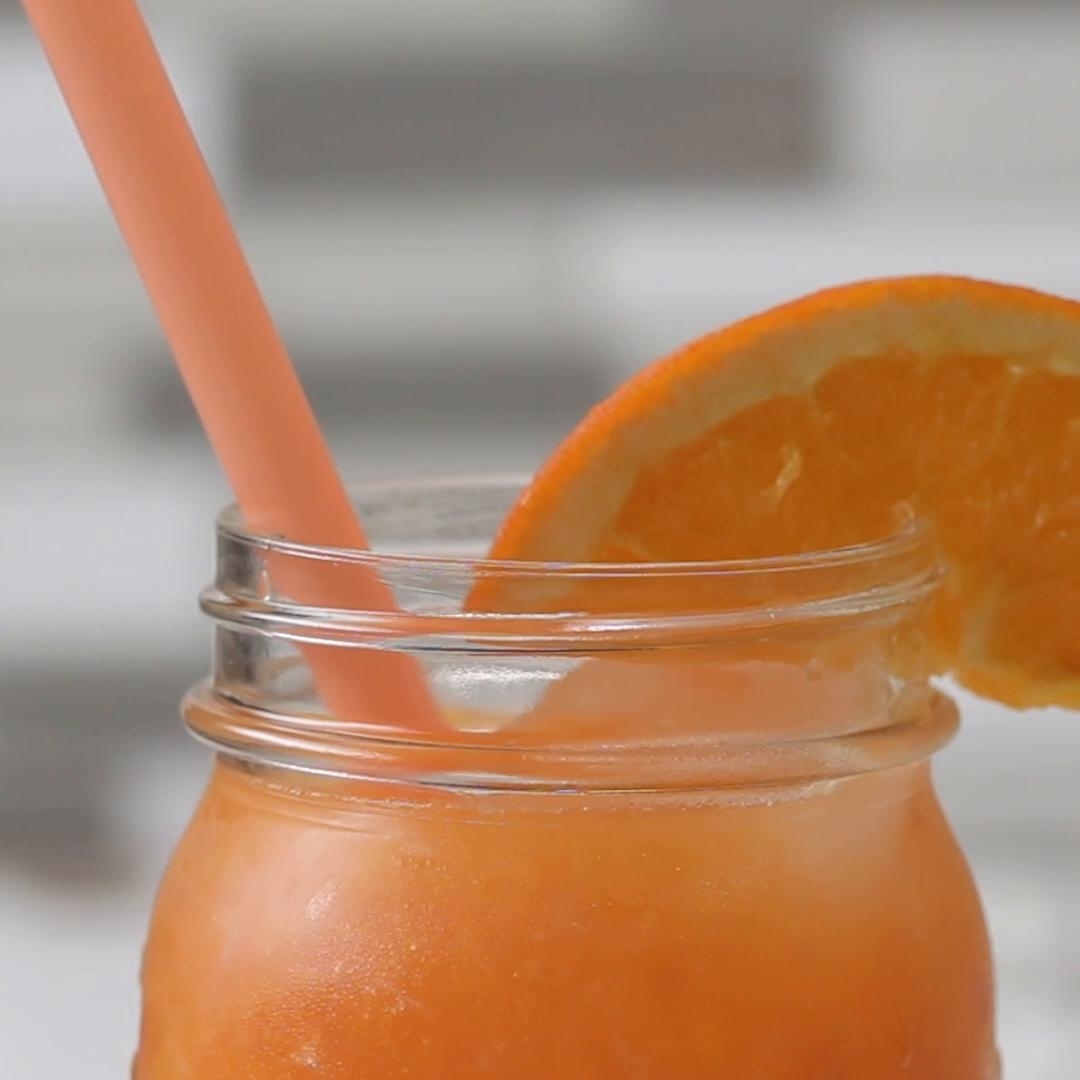 Jar of orange smoothie with a straw and garnished with an orange slice
