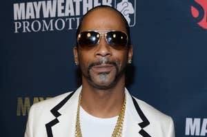 Snoop Dogg in a black and white blazer and sunglasses, posing in front of a promotional backdrop
