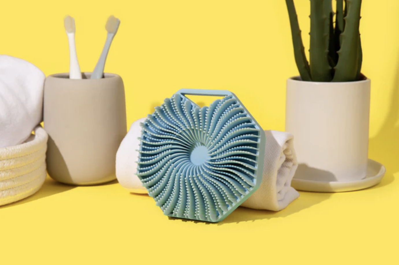Eco-friendly bathroom accessories including a loofah, toothbrushes, and a plant on a yellow background