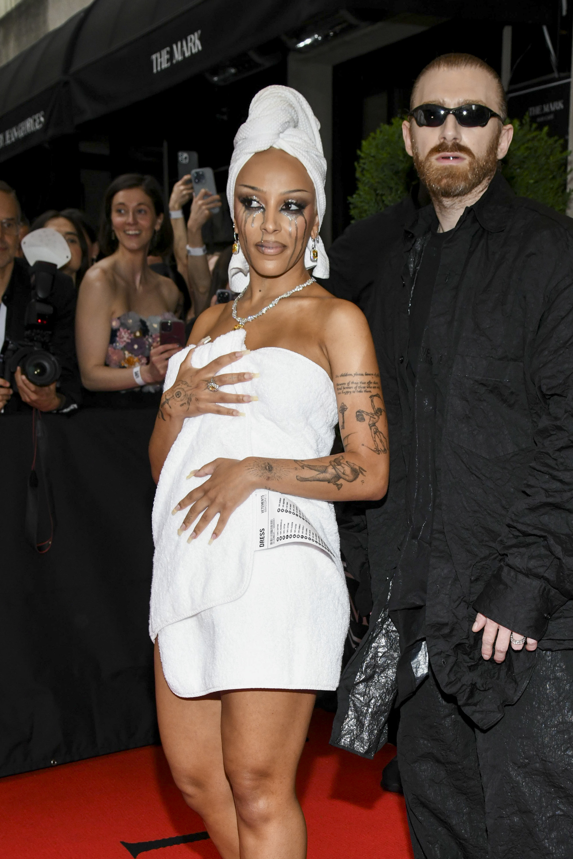 Rihanna in a white dress with a head wrap and A$AP Rocky in a black textured suit on the red carpet