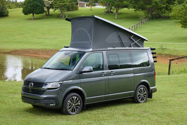 A Volkswagen van with a rooftop tent parked on a grassy field near a pond