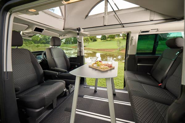 Interior of a van with seats and a table set up for dining, overlooking an outdoor scene