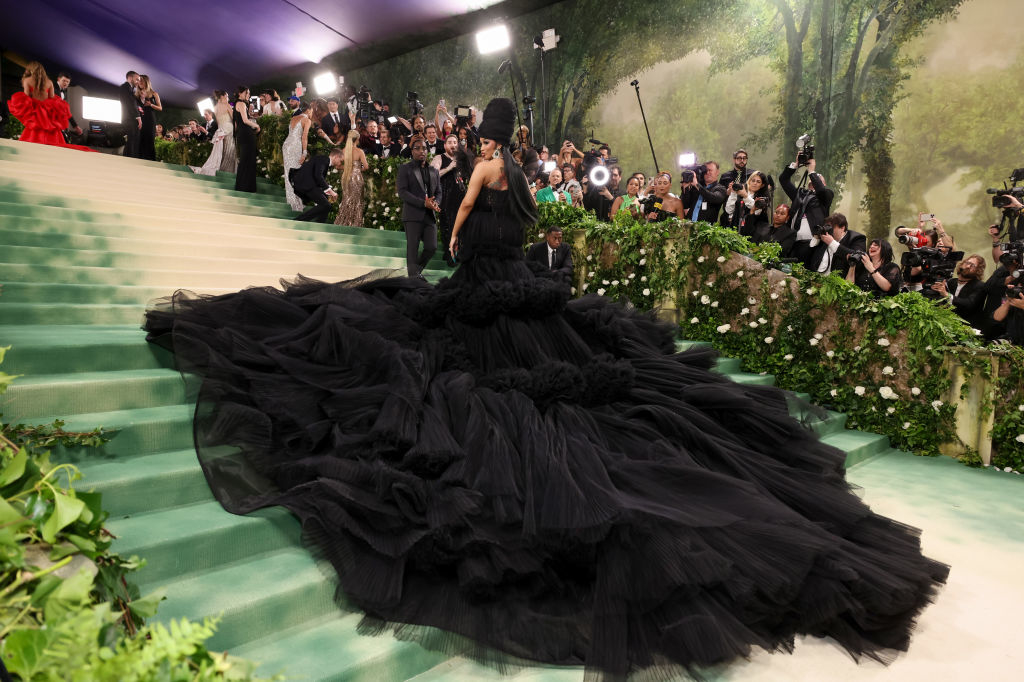 Cardi in an expansive gown with ruffled layers standing on stairs at an event, photographers in the background