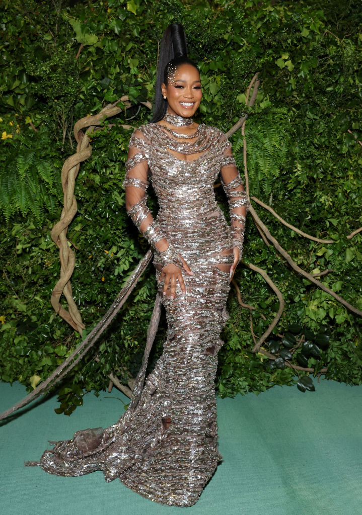 Keke Palmer stands smiling in a sparkling, long-sleeved gown with a high neck and train