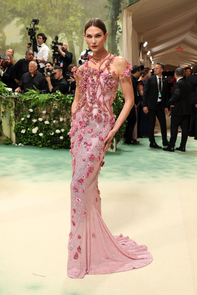 Karlie Kloss in a beaded floral gown posing on a carpet with photographers in background