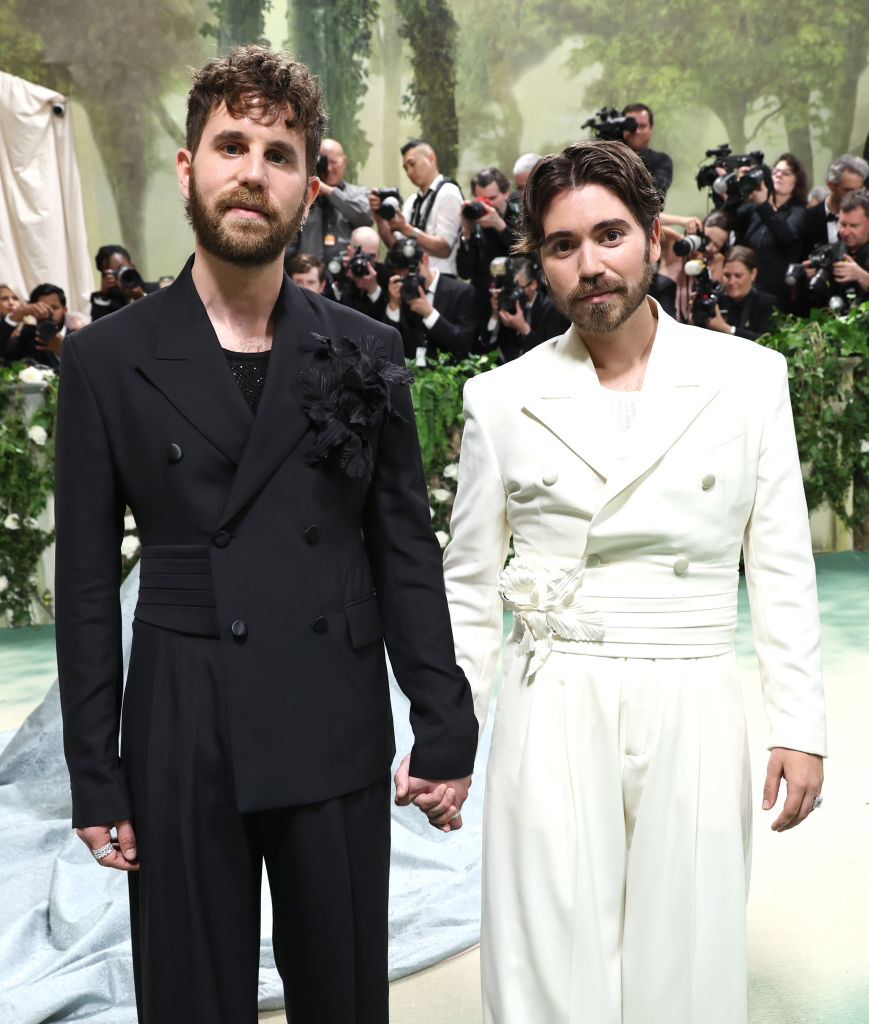 Ben in double-breasted suit with a floral adornment, Noah in belted suit, holding hands