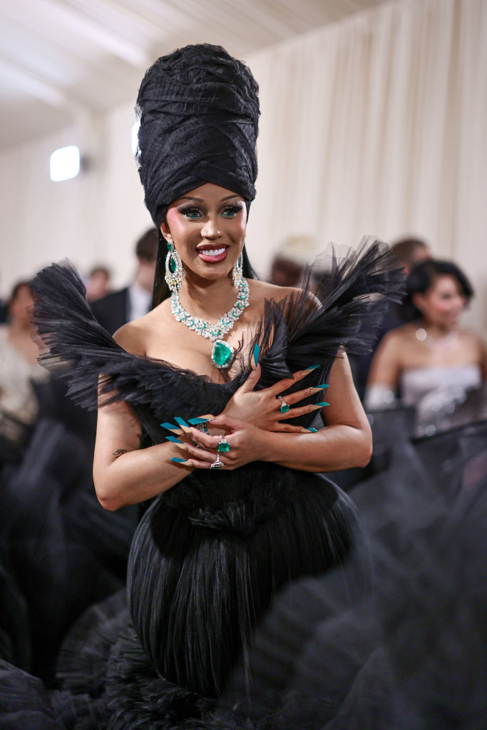 Cardi at an event wearing a feathered outfit with a large turban and statement jewelry
