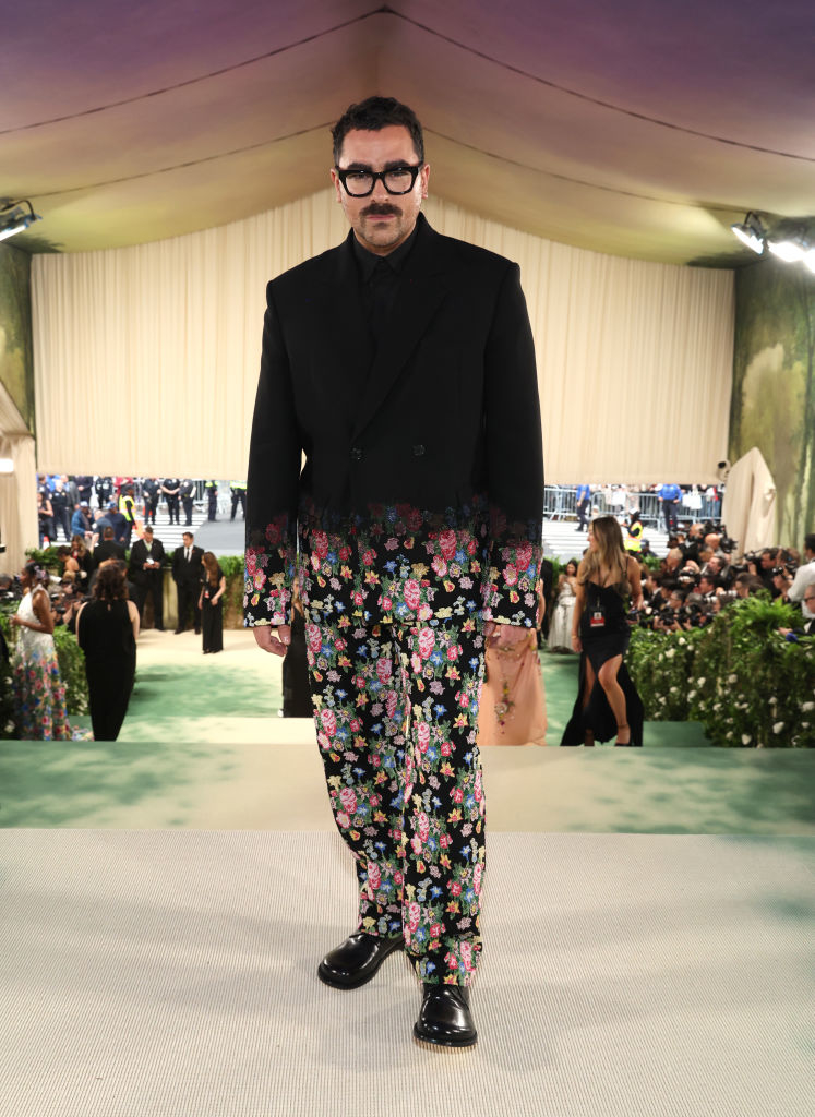 Man in a black jacket and floral trousers posing on a carpet at an event