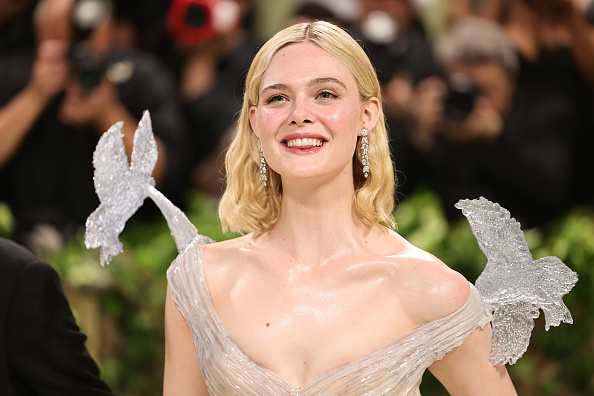 Elle Fanning smiling in a glittery dress with large butterfly appliqués on shoulders