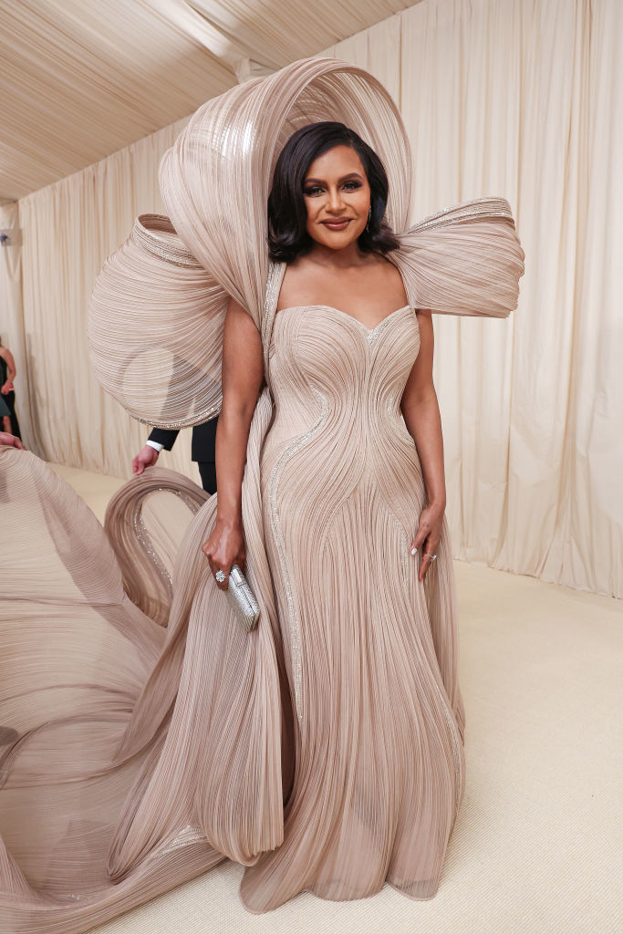 Mindy Kaling in a sculptural pleated gown and carrying a clutch at an event