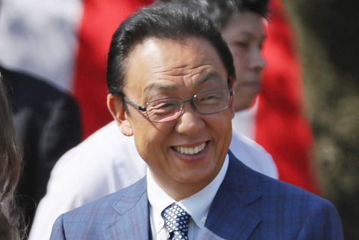 春のイベントに出席する笑顔の人々、梅沢富美男さんはスーツ着用、背景に旗