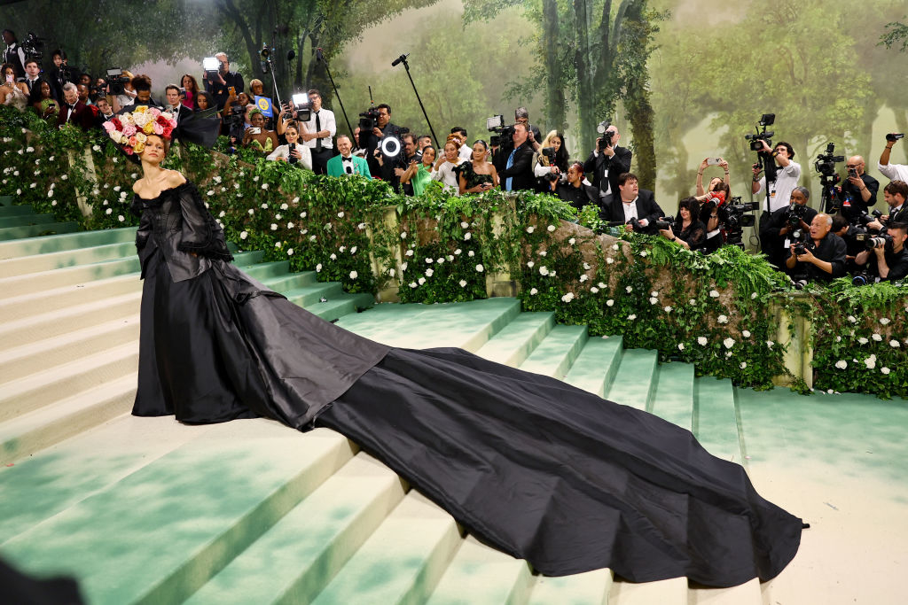 Zendaya in an extravagant gown with a long train, posing on a staircase at a high-profile event