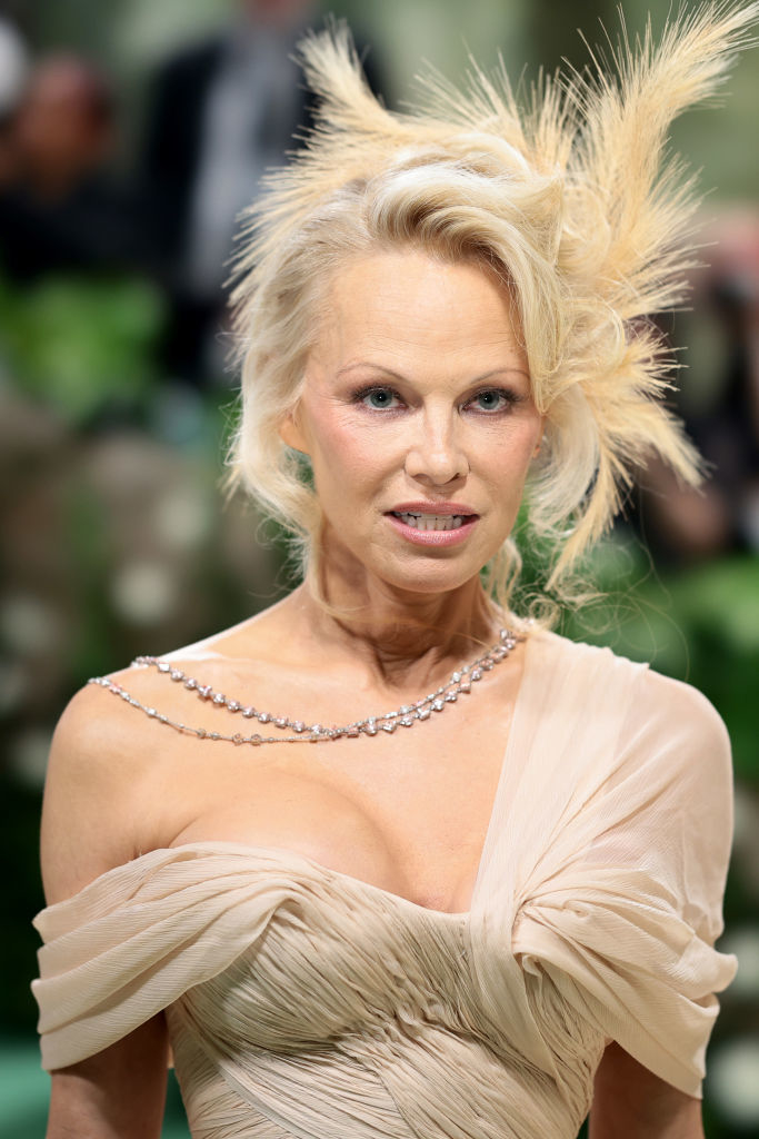 Pamela Anderson in a beige off-shoulder gown with feathered hair accessory