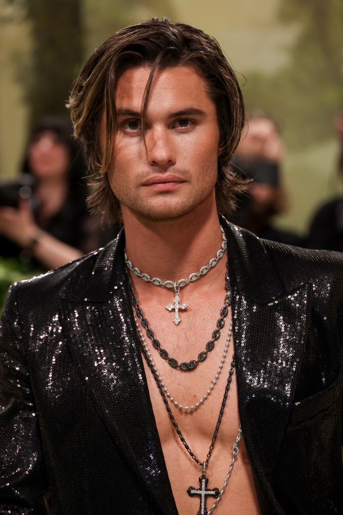Chase Stokes with medium-length hair wearing a sequined jacket and layered necklaces at an event