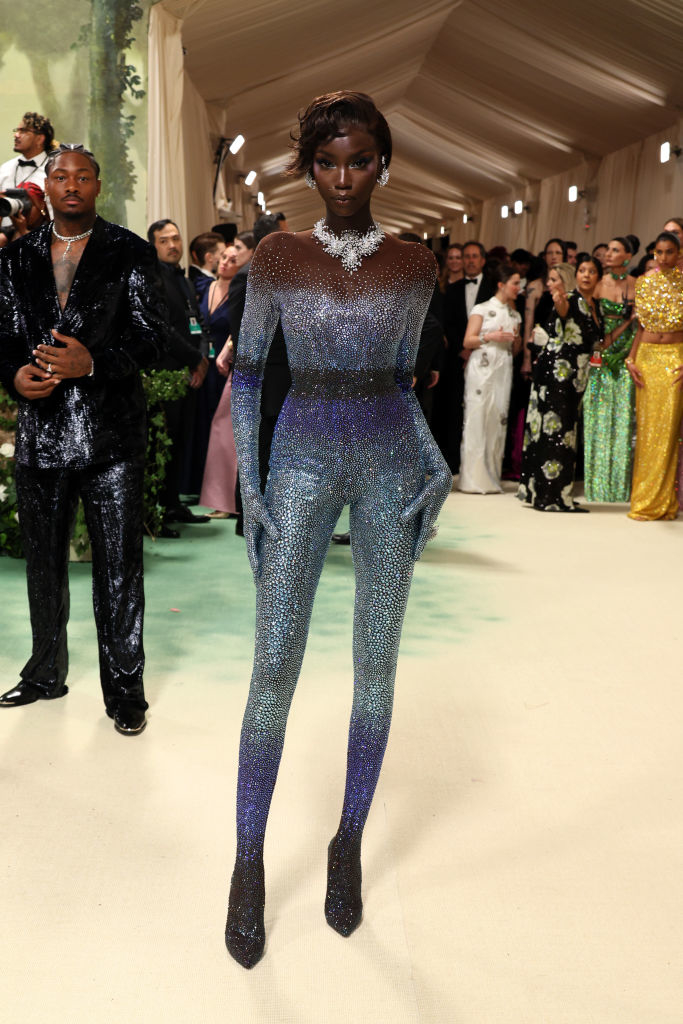 Model on runway in a shimmering bodysuit with gradient effect and diamond necklace