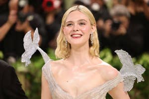 Elle Fanning smiles at an event wearing a sheer, shimmering dress with whimsical winged shoulders