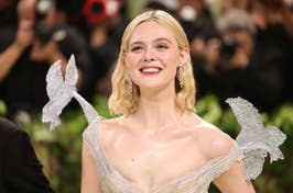 Elle Fanning smiles at an event wearing a sheer, shimmering dress with whimsical winged shoulders