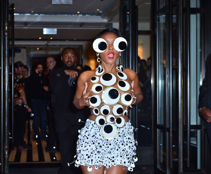 Person in a unique circular-patterned outfit and oversized round sunglasses exits a building