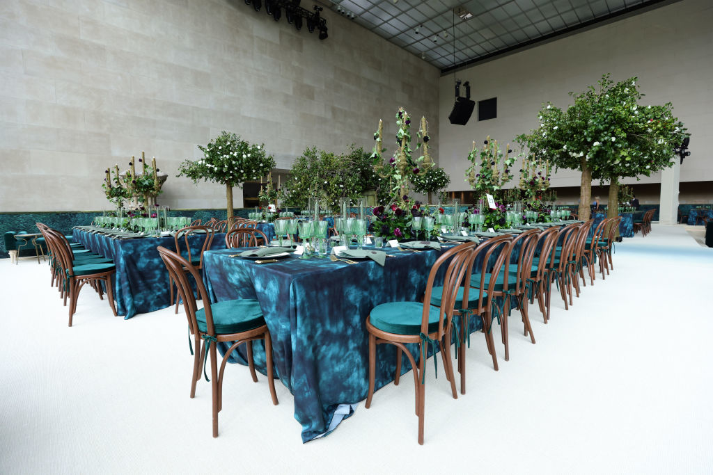 Elegant event setup with round tables draped in blue, floral centerpieces, and arranged wooden chairs