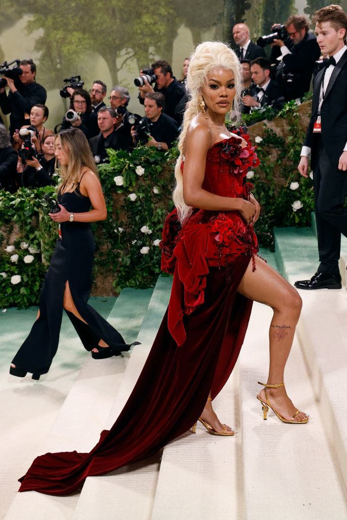 Person in an elegant red dress with floral applique poses on the stairs with photographers in the background