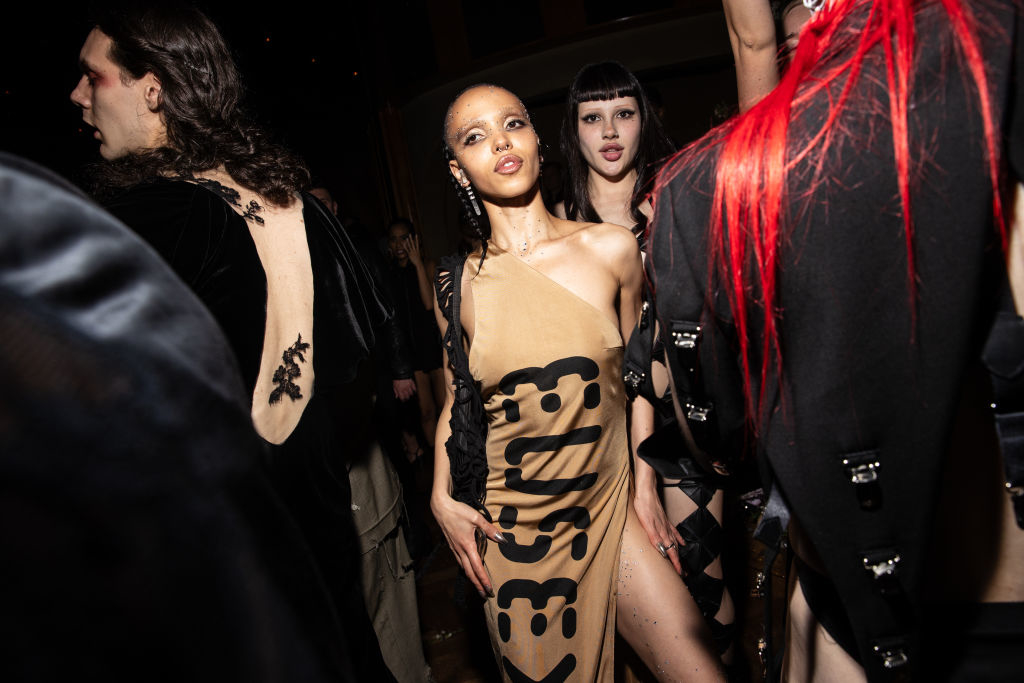 Three models backstage at a fashion show wearing avant-garde black outfits with bold cutouts