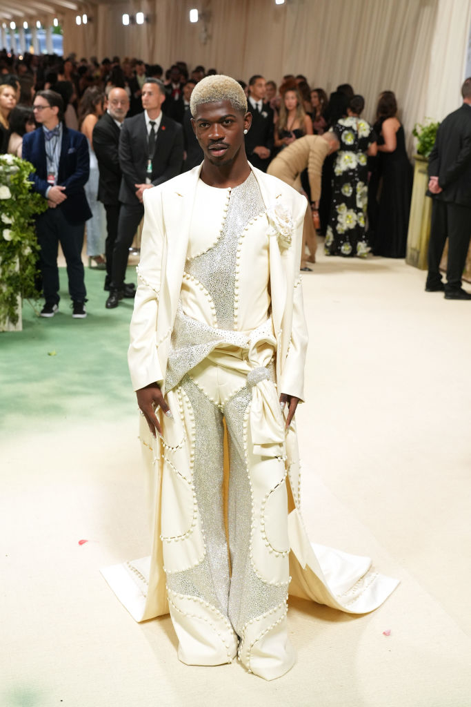 Man in elaborate white suit with silver patterns and matching cape at an event