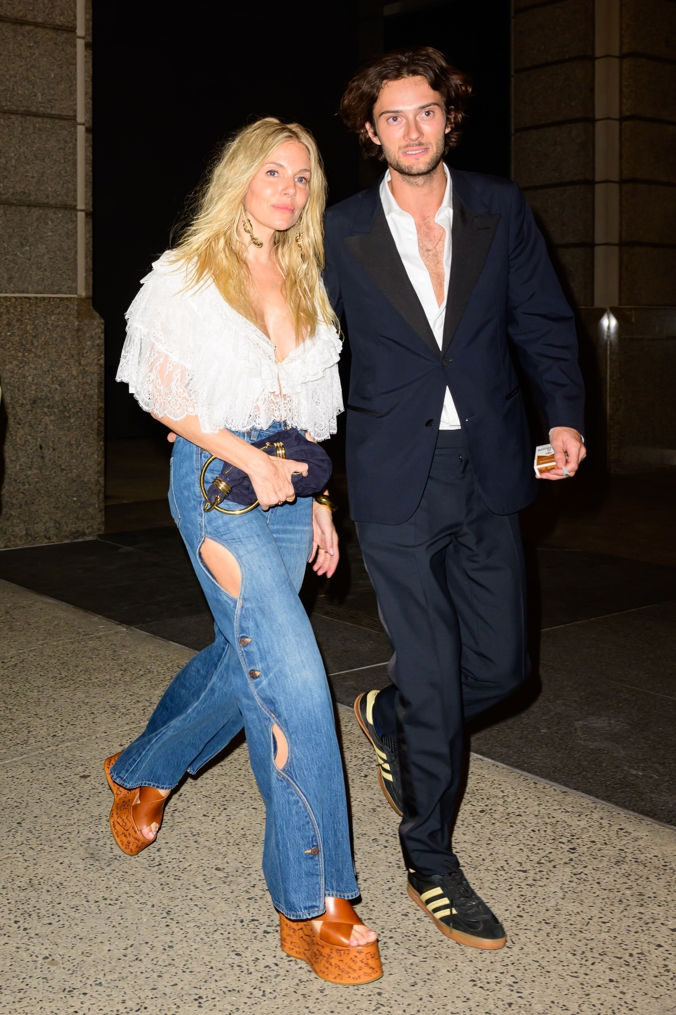 Two people walking, man in a suit holding a drink, woman in a white blouse and jeans