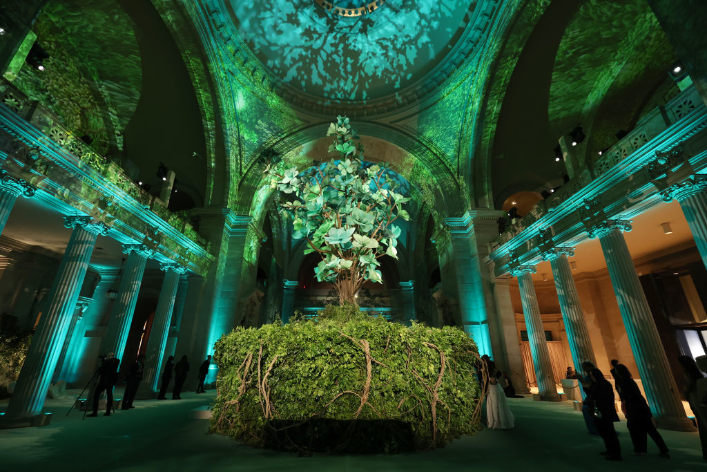 Elegant event space with a large central floral display and illuminated green projections on the ceiling. Guests in formal attire mingle nearby