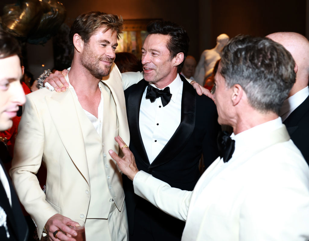 Men in formal wear smiling and chatting at an event; one in a white suit, another in a tuxedo
