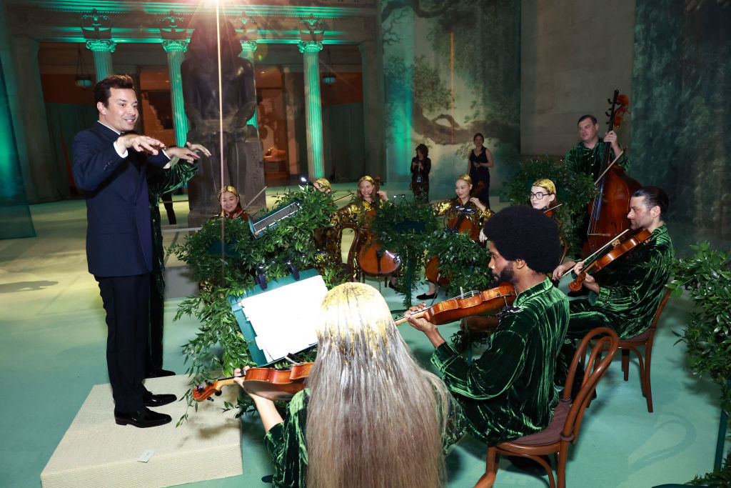 Jimmy Fallon conducts a small orchestra in a whimsical setup with greenery accents