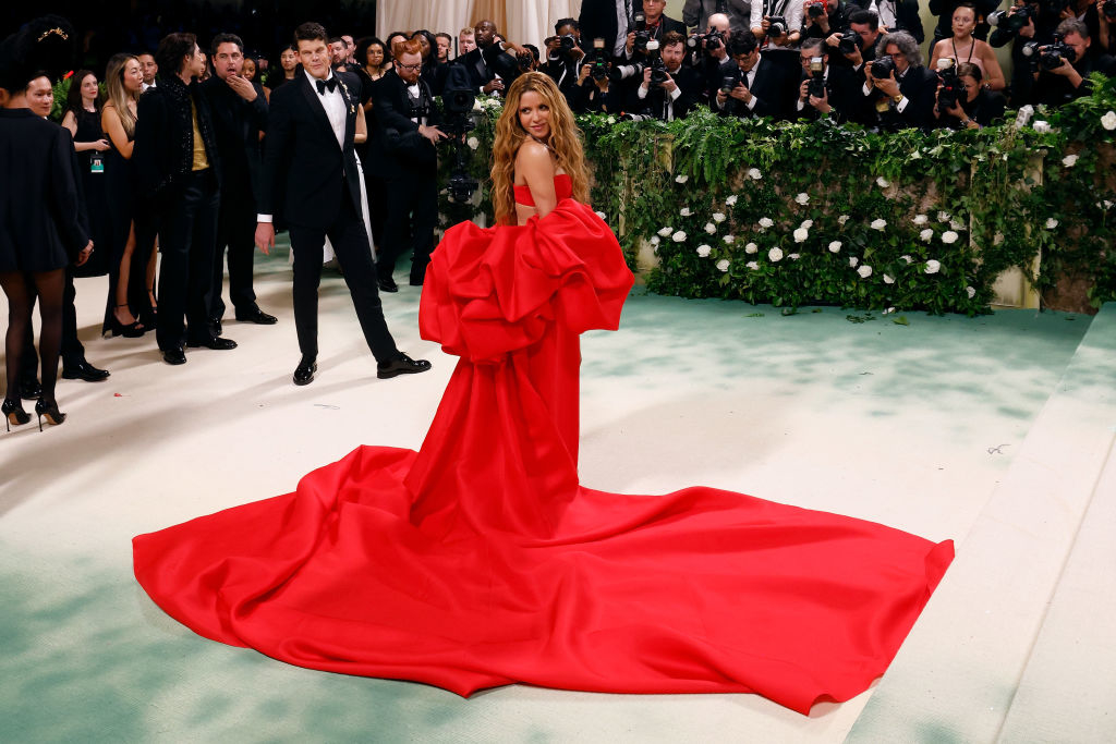 Person in a grand red gown with a bow on the carpet, photographers in the background